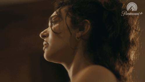 A woman looks upward in profile in a dark, cinematic scene.