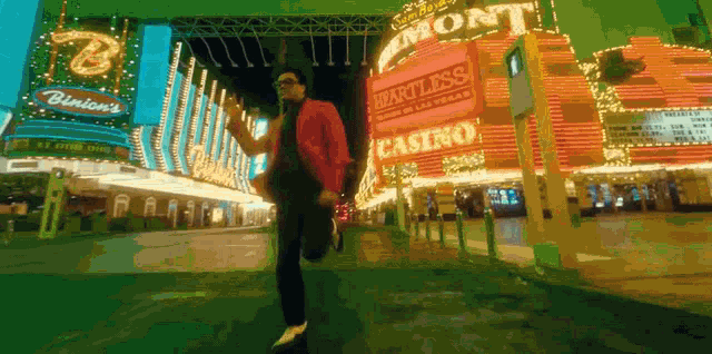 a man in a red jacket is running in front of a heartless casino sign