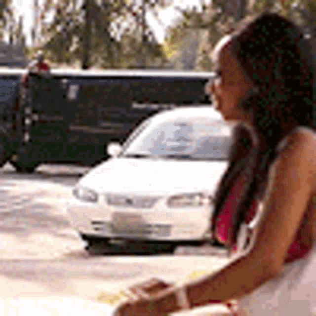 a woman is sitting in front of a white car on a street .