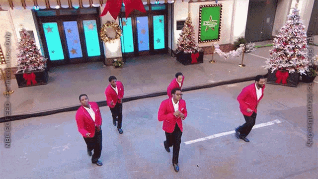 a group of men in red jackets are dancing on a street in front of a building that says abc