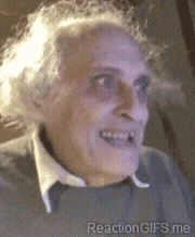 An older man smiles eerily in a dim grainy video.