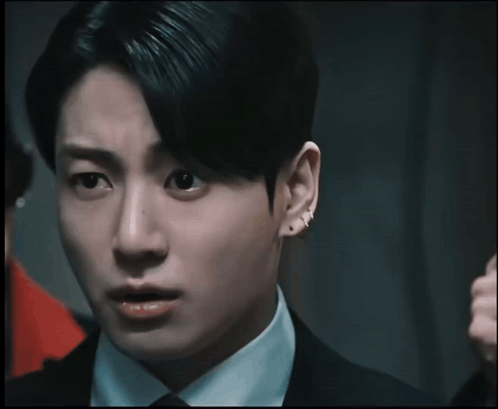 Jungkook looks wide-eyed in a dramatic dark close-up.