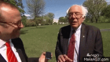a man in a suit and tie is talking to another man in a park