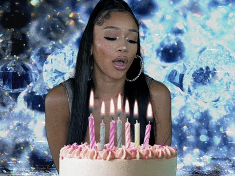 A woman blows out candles on a large birthday cake.