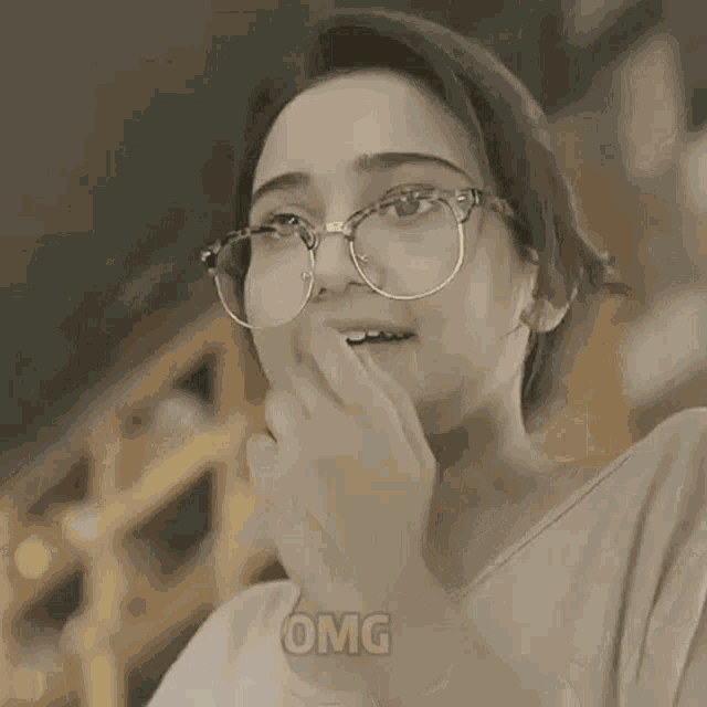 a woman wearing glasses is covering her face with her hands and the word omg is above her head