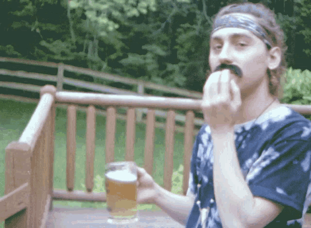 a man with a mustache is holding a glass of beer and eating something