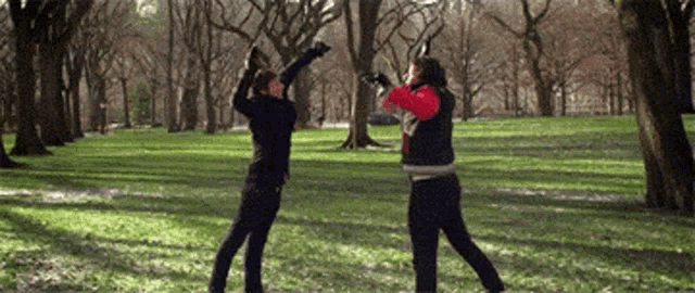 Two people in a park slowly bring their raised hands together for a high five.