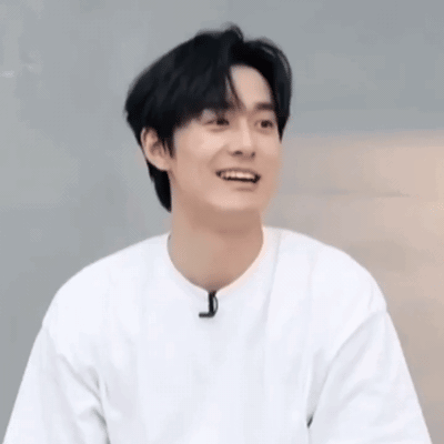 a young man wearing a white t-shirt is smiling and looking at the camera .