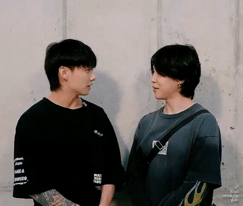 Two men in dark shirts stand facing each other in conversation.