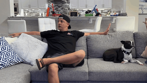 A person lounges on a couch while a dog sits nearby.