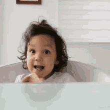 A smiling toddler in a bathtub raises a thumbs up.