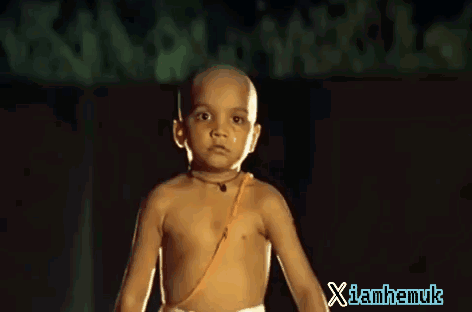 A child stares seriously toward the camera in a dim scene.