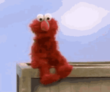 Elmo looks uneasy on a ledge under a bright sky.