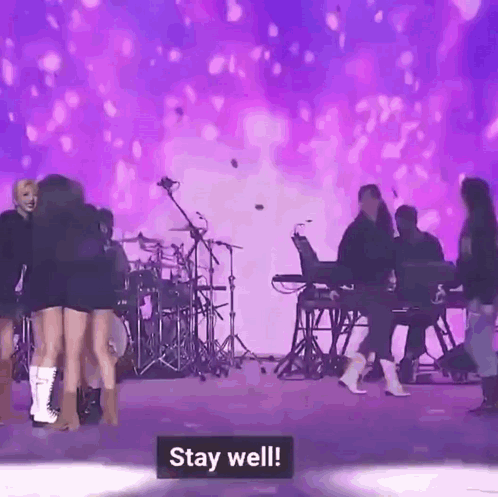 a group of women are standing on a stage with a purple background and a sign that says `` stay well '' .