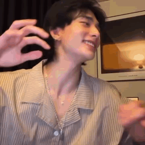 a young man wearing a striped shirt and a necklace is smiling and making a face .