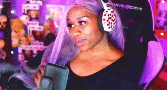 a woman with purple hair is wearing headphones and sitting in a dxracer chair