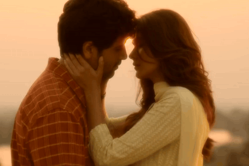 A couple stands forehead-to-forehead in golden sunset light.