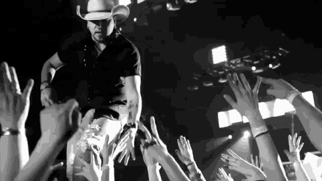 a man in a cowboy hat stands in front of a crowd of people raising their hands