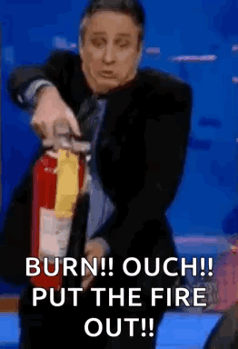 Jon Stewart uses a fire extinguisher as the caption shouts “BURN!! OUCH!! PUT THE FIRE OUT!!”
