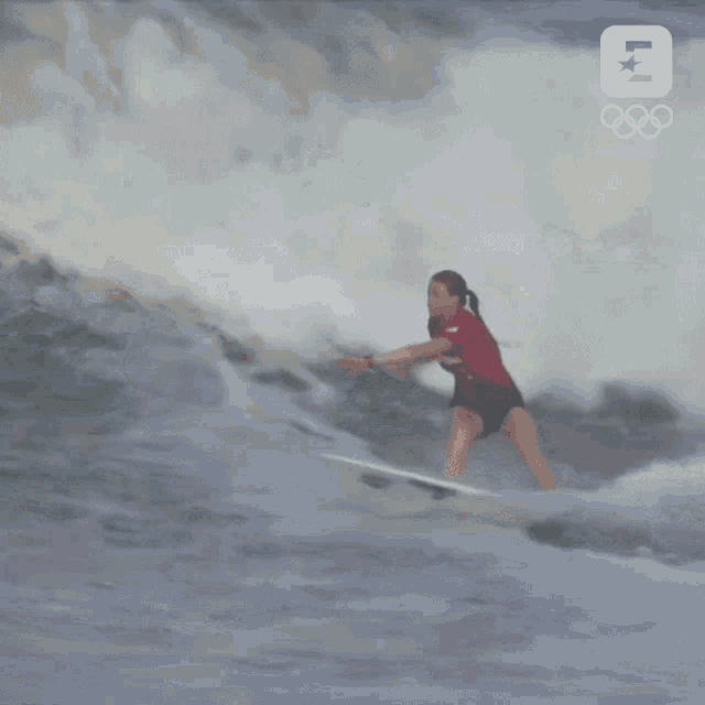 a surfer is riding a wave with the olympics logo behind her