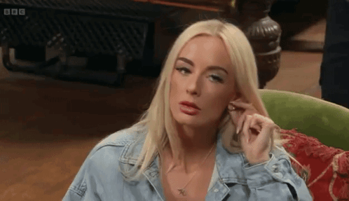 A blonde woman rolls her eyes while seated indoors.