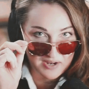 A woman lowers red sunglasses and stares directly at the viewer.