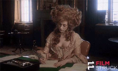 a woman in a wig sits at a desk in front of a sign that says film stuck