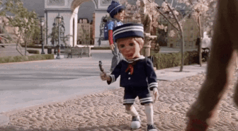 a doll in a sailor outfit is walking down a sidewalk holding a stick
