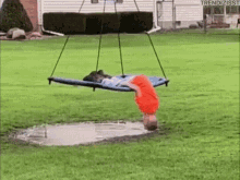 A person hangs upside down from a playground swing over a puddle.