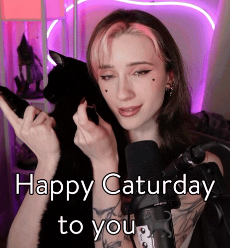 a woman with pink hair is holding a black cat and the words happy saturday to you