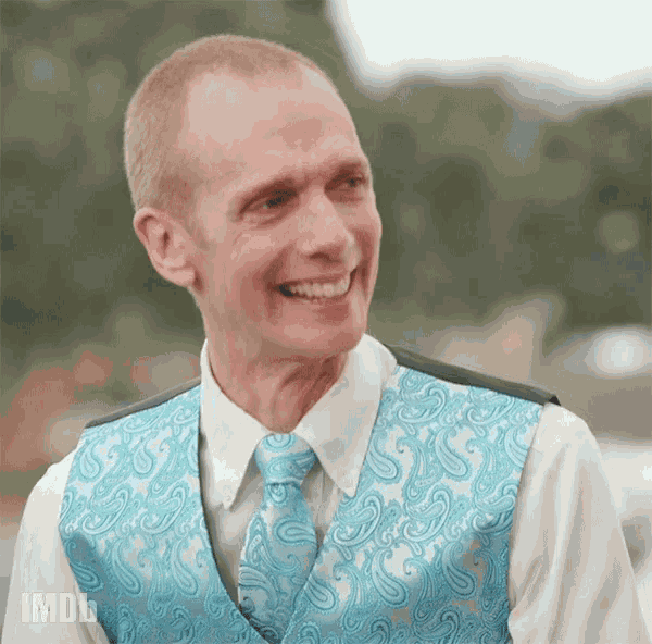 a man in a blue paisley vest and tie is smiling ..