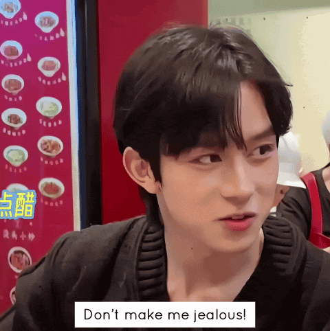 a man is sitting in front of a sign that says don 't make me jealous