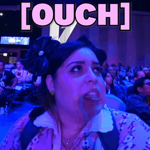 A woman at an event looks startled beneath a large “[OUCH]” caption.