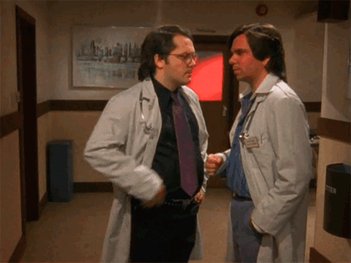 two doctors are shaking hands in a hallway in front of a sign that says emergency