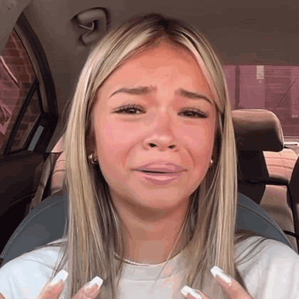 A blonde woman in a car looks distressed and close to tears.