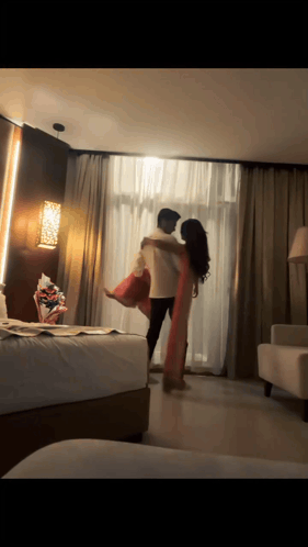 A couple hugs in a warmly lit hotel room.