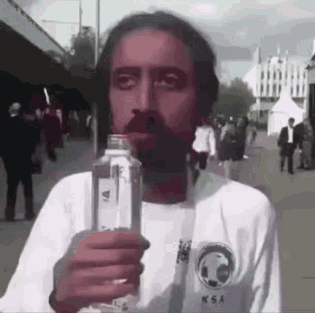A man drinks water with a shaky, nervous expression outdoors.