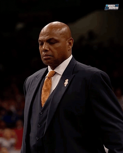 A basketball coach in a suit looks off to the side with concern.