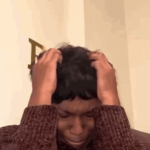 a man in a sweater is holding his head in pain .