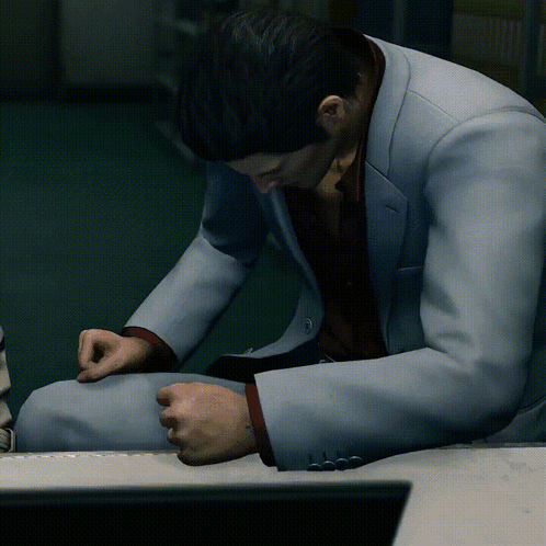 a man in a suit sits on a desk with his hands folded