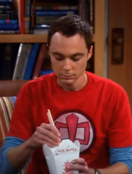 Sheldon Cooper eats from a cup with chopsticks while looking down.