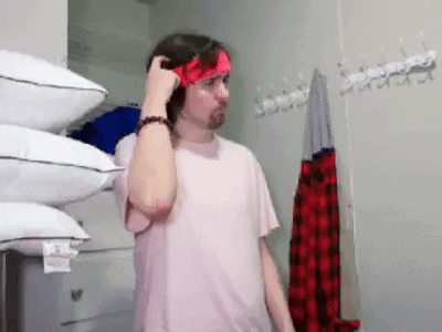 a man wearing a pink shirt and a red headband is standing in front of a pile of pillows .
