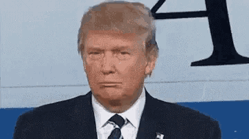 Donald Trump looks forward in a debate setting with a blank expression.