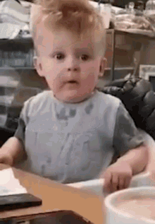 A toddler looks up in surprise while seated at a table.
