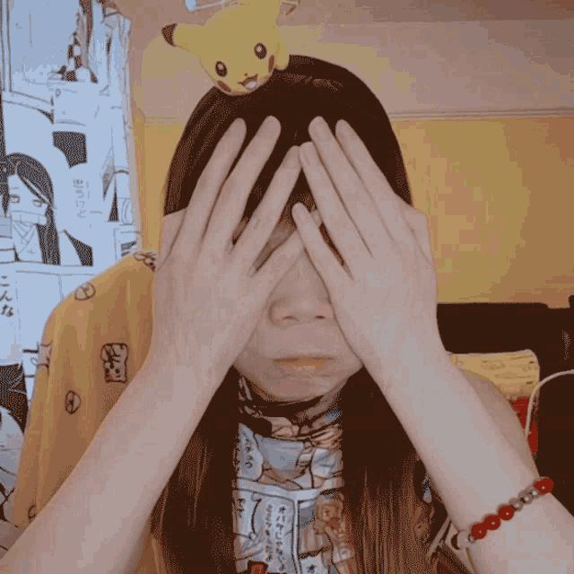 a woman covering her face with her hands and a pikachu on her head