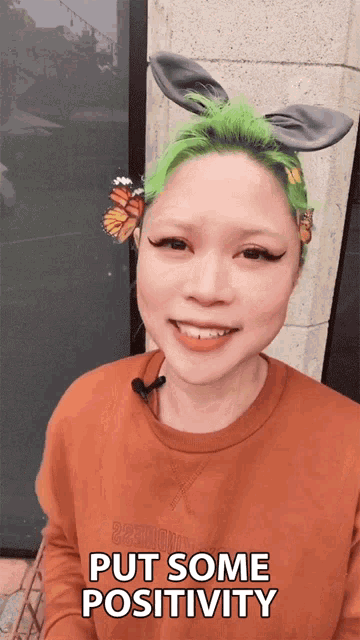 a woman with green hair has a butterfly in her hair and says " put some positivity "