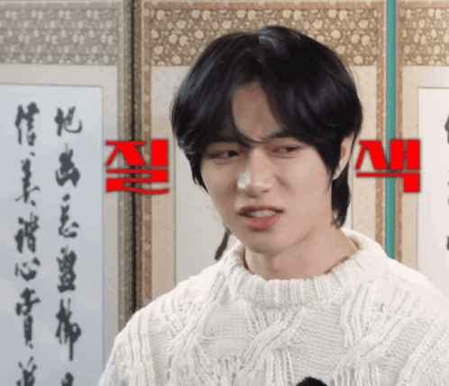 a man wearing a white sweater is standing in front of a wall with chinese writing on it
