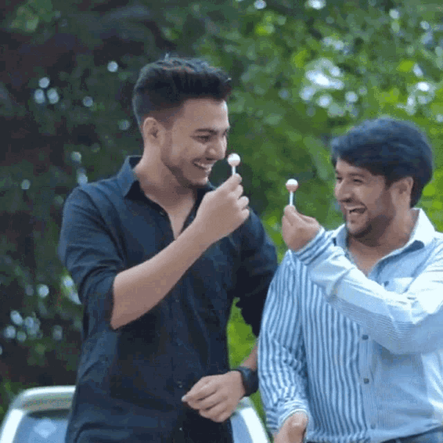 two men are standing next to each other one is holding a lollipop in his hand