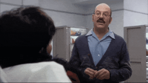 a bald man with glasses and a mustache is talking to another bald man