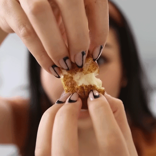a woman with black and white nails holds a piece of food in her hands